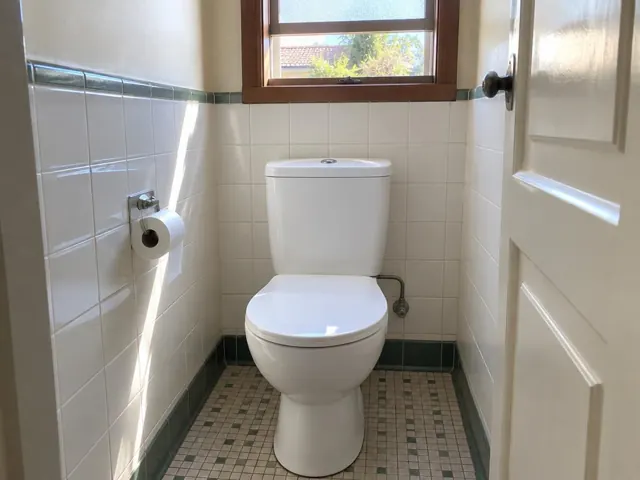 Clean white toilet in a tiled bathroom with a window and patterned floor in Lidcombe