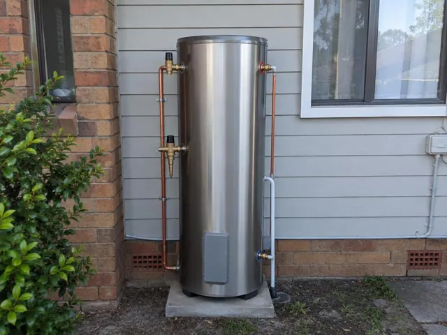 Outdoor stainless hot water cylinder beside brick and weatherboard walls with neat copper pipework in Chester Hill