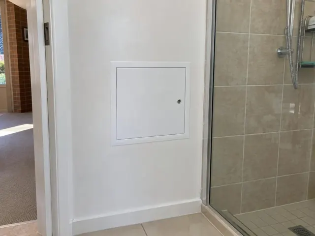 Small white access panel in a painted bathroom wall beside a tiled shower in Sefton